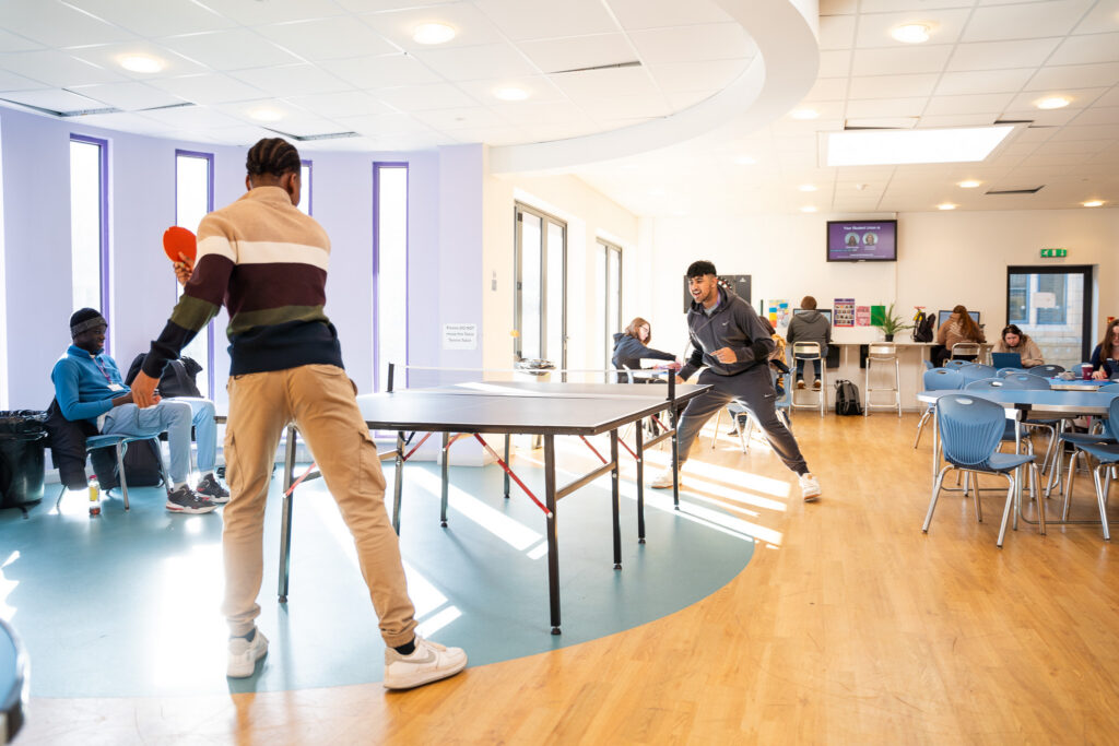 Two students play table tennis in a common room while others sit at tables, Prior Pursglove College.