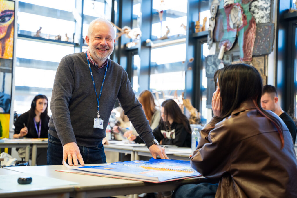 A tutor smiling as he talks a student through a portfolio in the art studio
