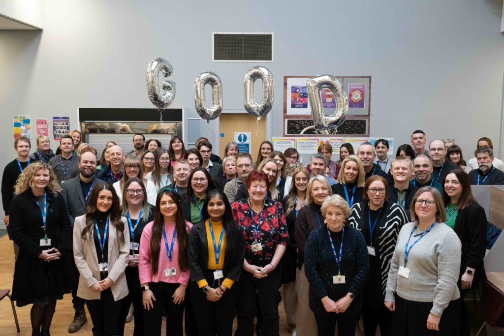 Staff stand together for a group photograph under balloons spelling the word good, Prior Pursglove College.