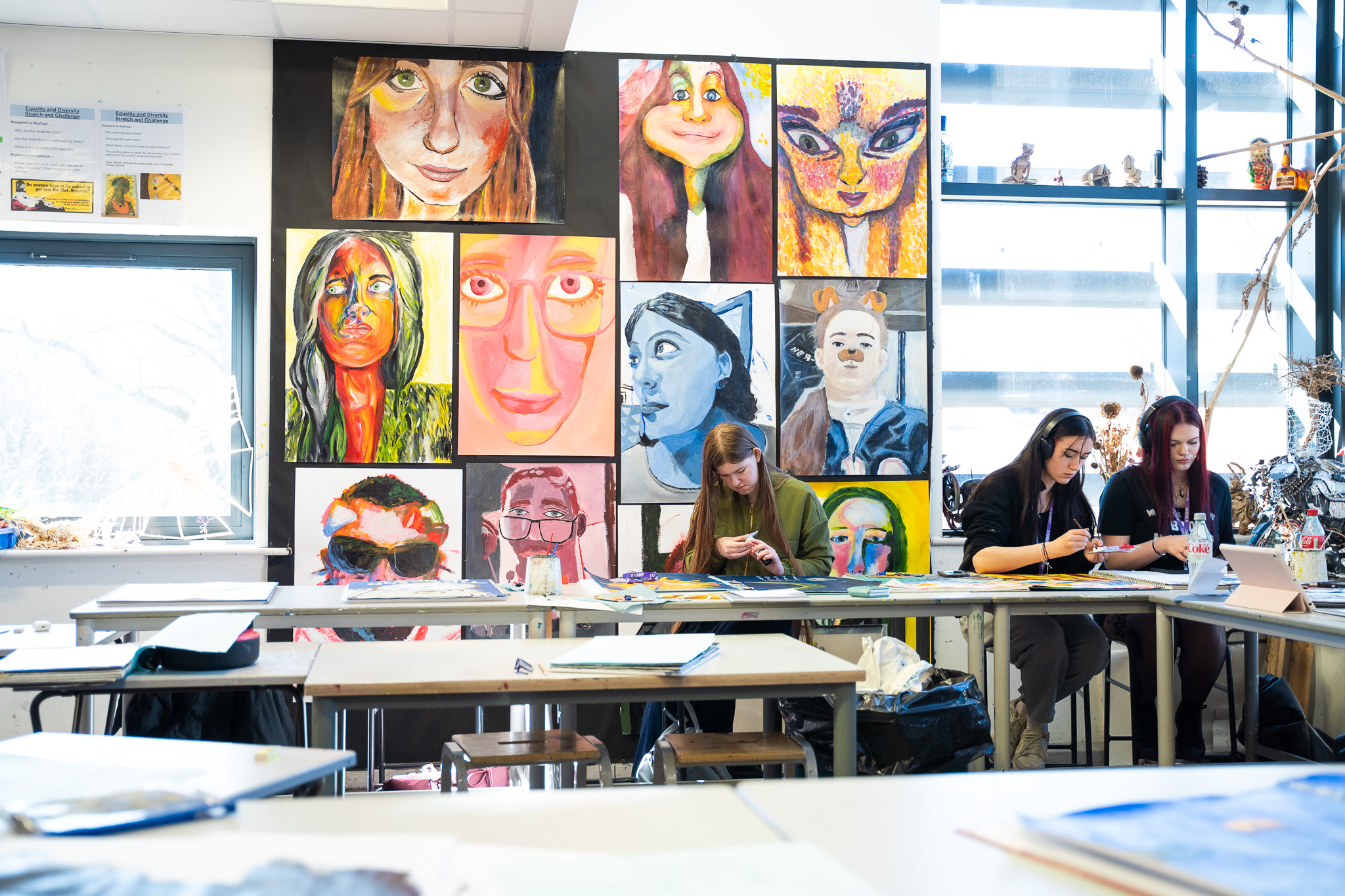 Students working below a wall of painted portraits