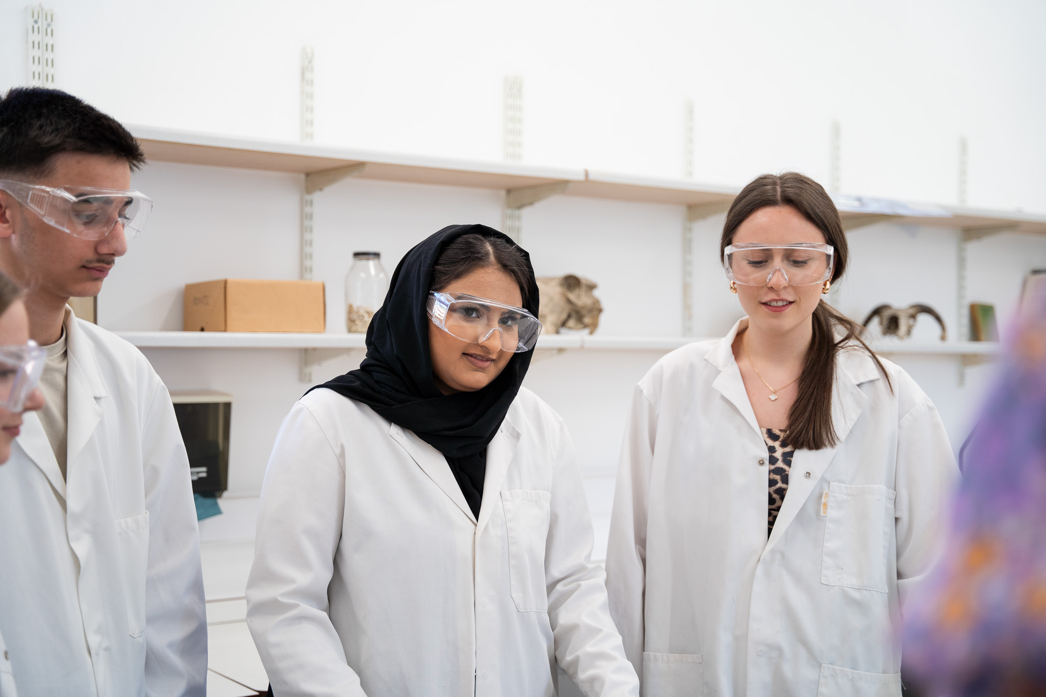 Three students in a biology practical wearing goggles and lab coats