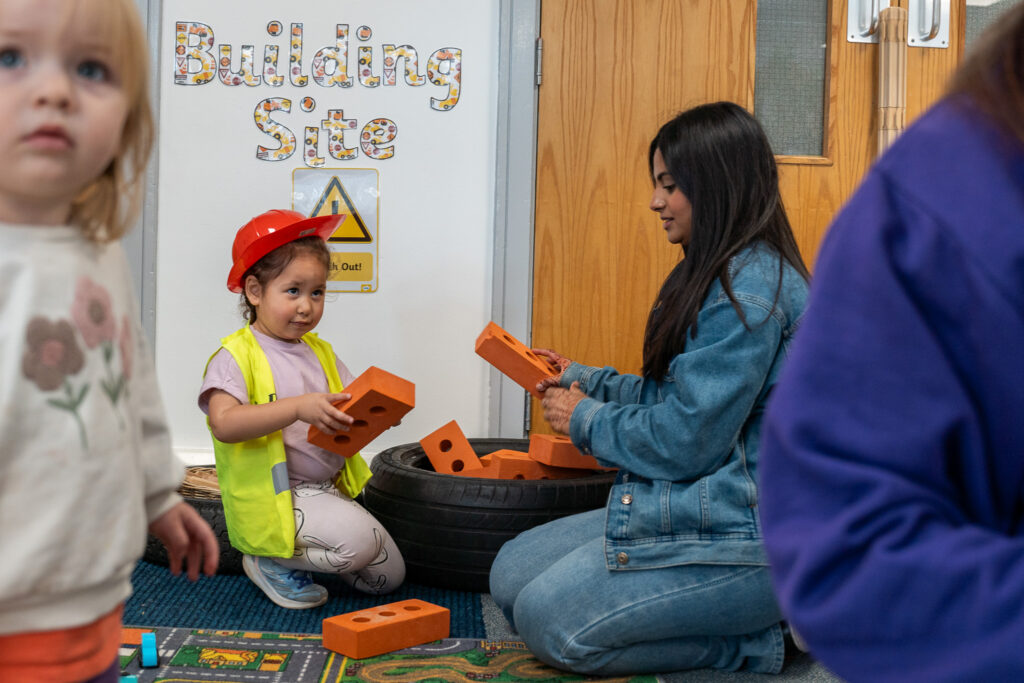 A young child in a hard hat in a building-site role-play area