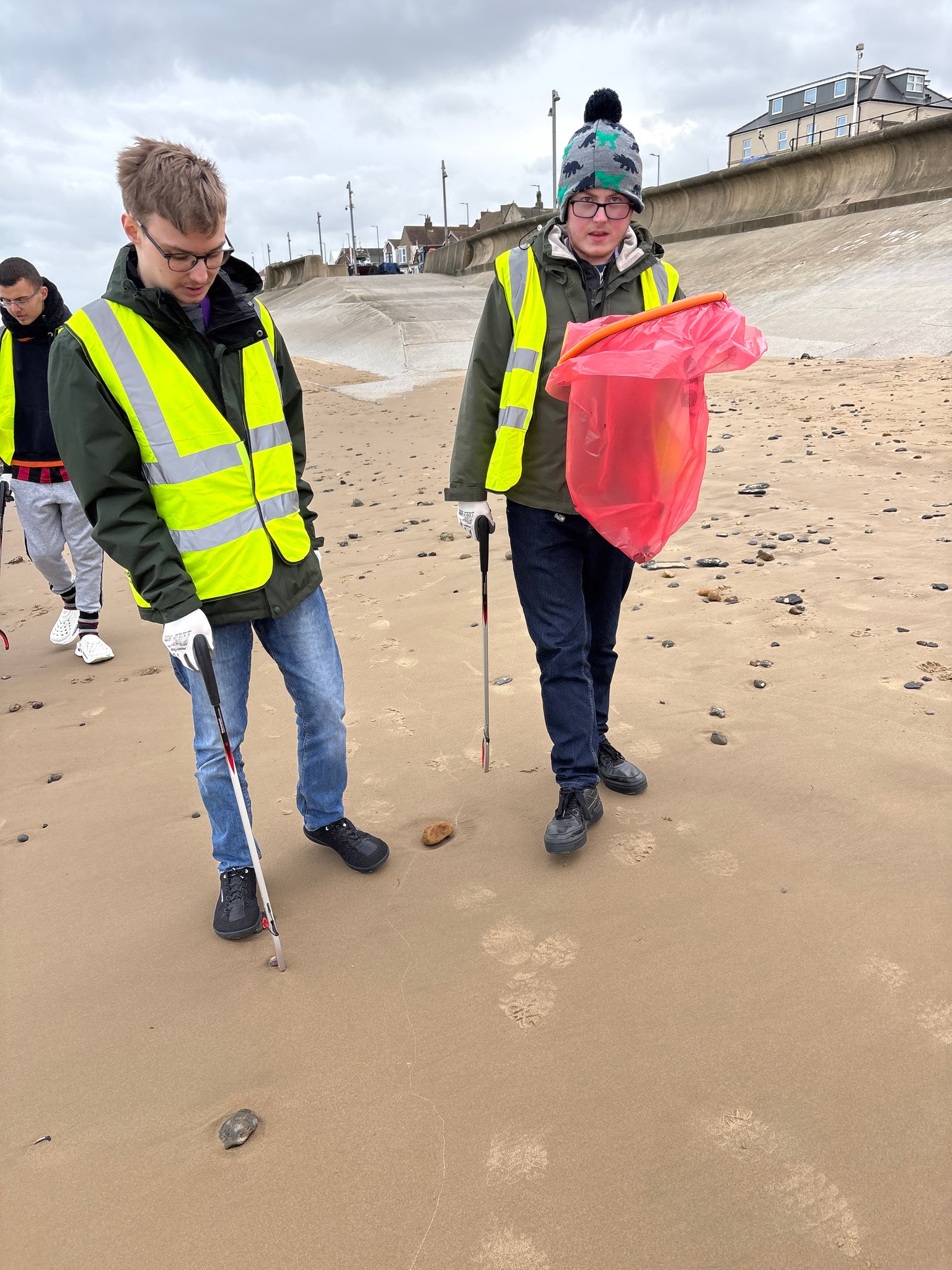 Two students with litter pickers and a bag on the beach at Redcar