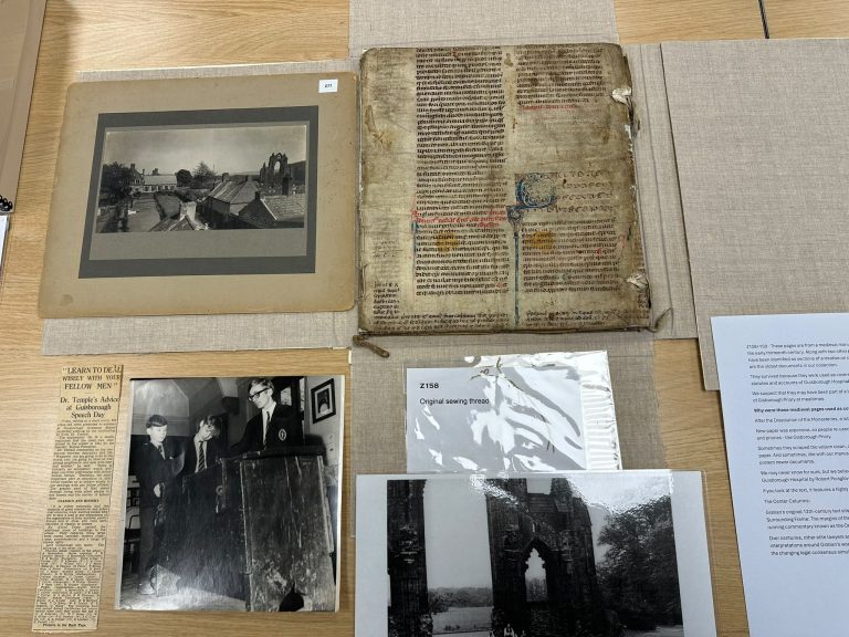 Items from the college archive laid out on a table, including an old handwritten manuscript, newspaper cuttings and historic photographs