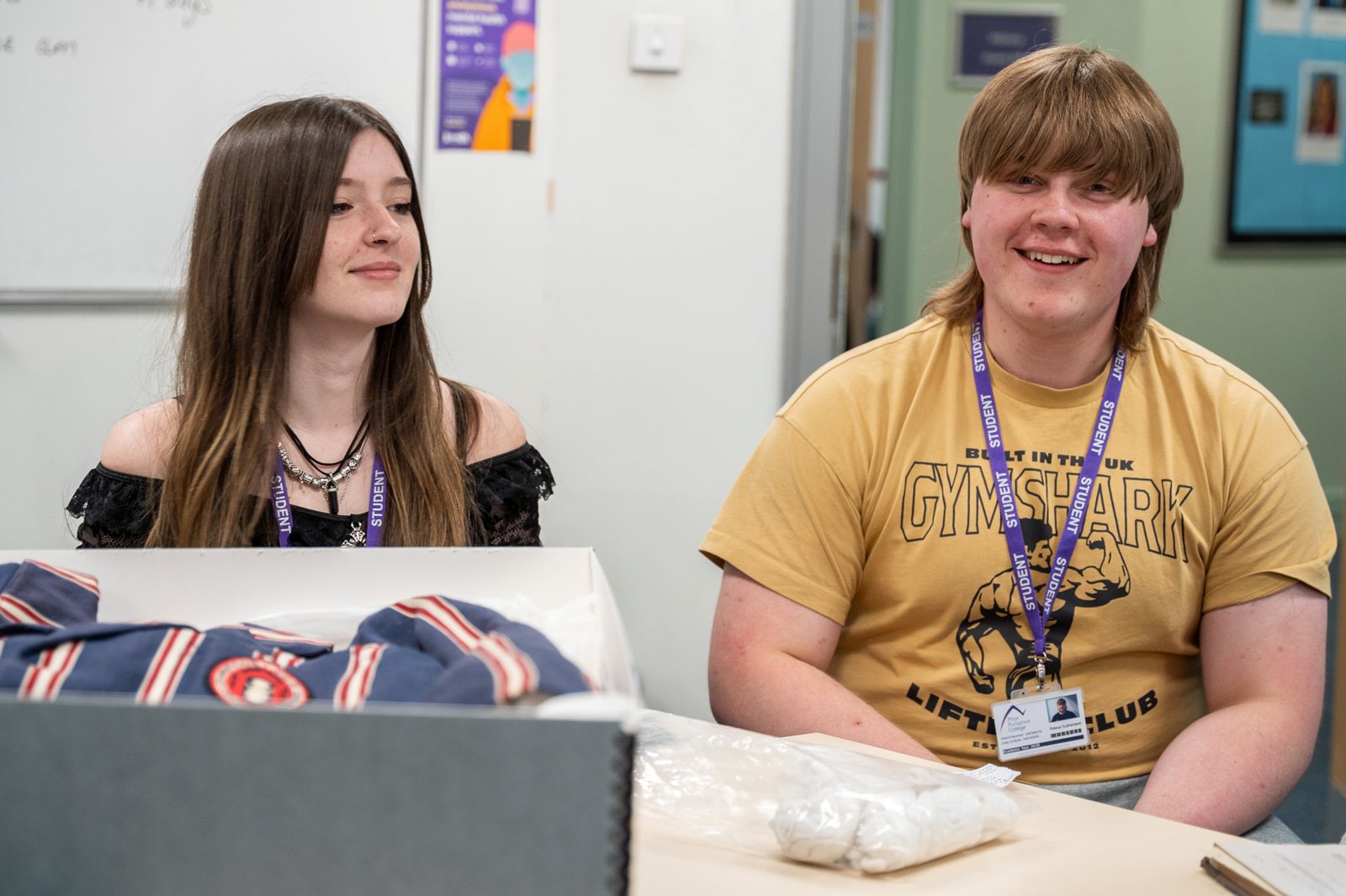 Two students smile as they sit together at a classroom table.