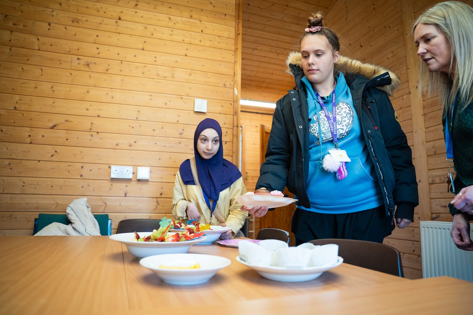 Students and a member of staff set out bowls of fruit salad on a table.