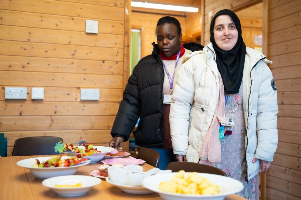 Two students stand beside a table of fruit and snacks they have prepared.