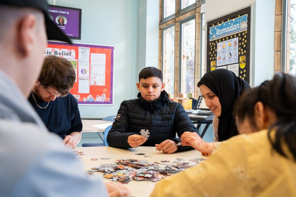 Students work together on a large jigsaw puzzle around a table.