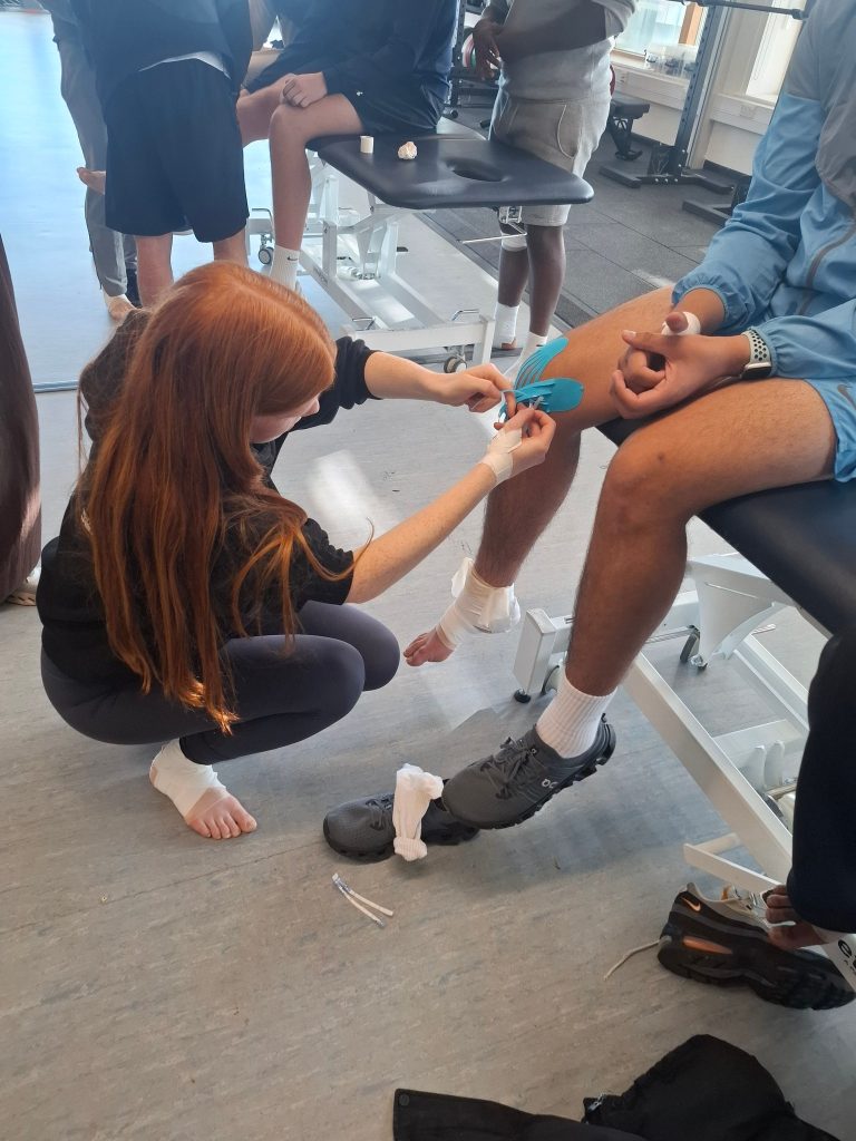 Students practise taping a knee with kinesiology tape
