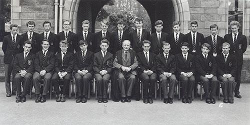 Geoff Farrington and a class of students in blazers in two rows in front of the Waterhouse arch, 1963.